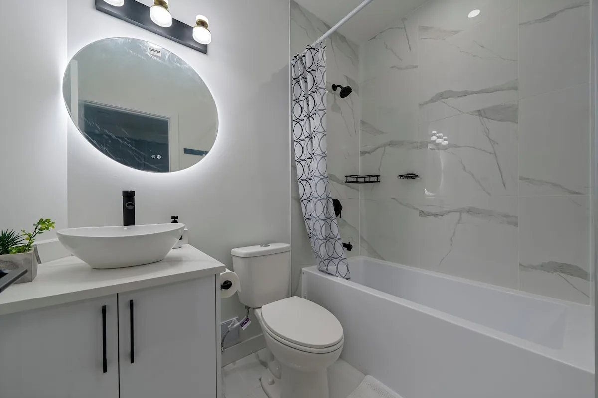 Full bathroom with LED mirror and marble-tiled tub and shower